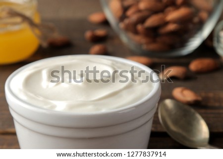 Greek yogurt in a ceramic bowl close-up with almonds and honey next to a spoon on a brown wooden background. healthy food. natural yoghurt. breakfast.