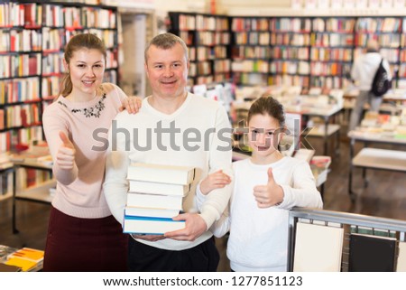 Happy family with preteen daughter holding pile of books bought in bookstore
