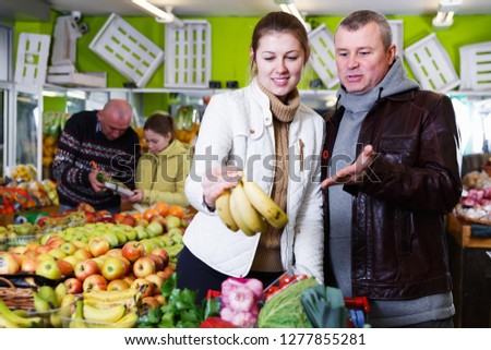 Positive young couple choosing fresh yellow bananas in fruit store. Focus on man