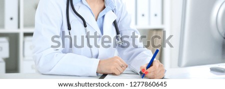 Unknown female doctor working at the desk with clipboard in hospital and filling up medical history form, close-up view. Medicine concept