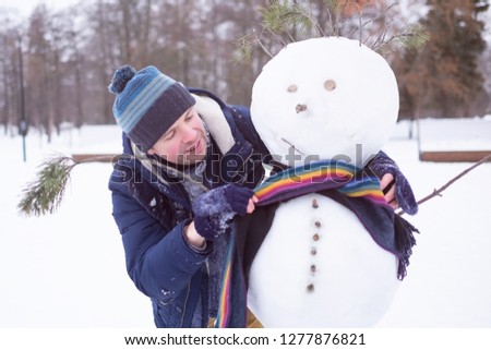 Young european man in warm clothes making snowman from snow outdoor. Having fun like a child at winter vacation.
