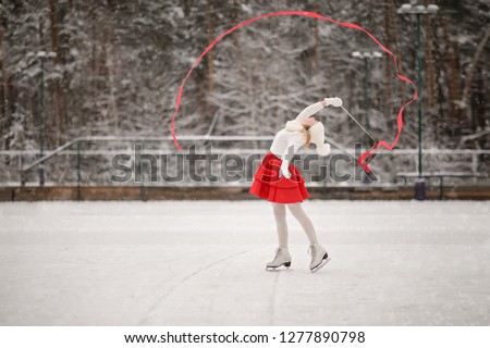 Child young girl ice skating at the ice rink outdoor. The girl in the red skirt