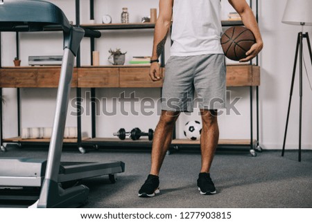 cropped view of tattooed man holding basketball in living room 