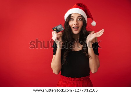Photo of a beautiful young woman standing isolated over red wall background holding credit card.