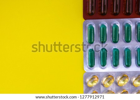 Capsules with medication in blister pack on yellow uniform background view from above with the clear area of half photo for labels, headers. Concept photo of pharmaceutical and natural herbal medicine