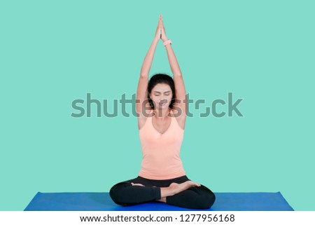 Picture of young Indian woman lifting hands while doing yoga exercise in the studio