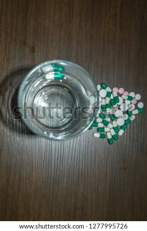 glass of water for take remedies - medicine drug pills in green, white and pink color, several sizes, on wood background health, supplement, hypochondria concept