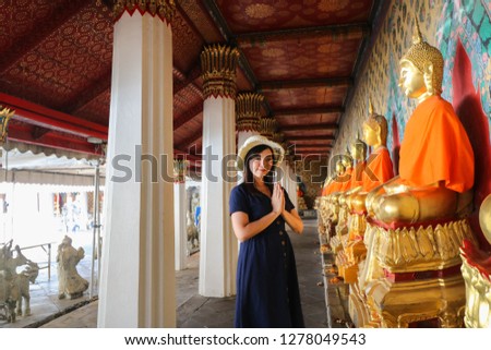 Asian beautiful girl wearing blue dress with white hat pray to the Buddha at Wat Arun in Bangkok, Thailand. Wat Arun is a famous tourist destination of Thailand. Travel concept