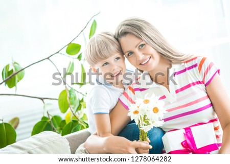 Mother and son together closeup portrait. Mothers day picture with copy space. Family indoors happy. Smiling mom with her child holding present and flowers.