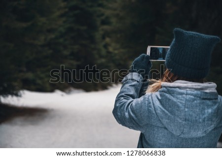 Winter travelling concept - back view woman taking picture of winter forest by smartphone 