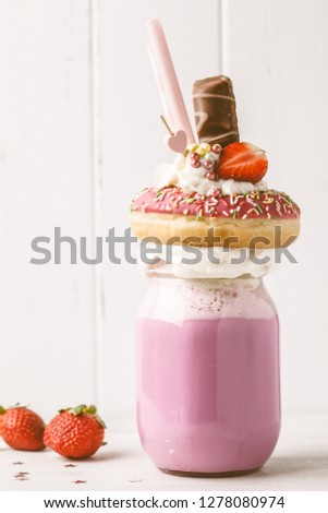 Pink strawberry Freak Shake cocktail with donut and sweets on a white background. Unhealthy desserts concept.