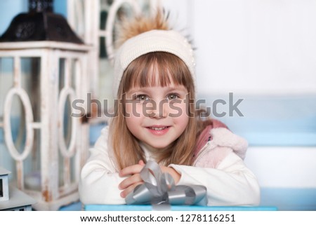 Merry Christmas, happy holidays! New Year. portrait of little cute girl in hat sitting on porch of house winter. child sits on wooden staircase on terrace. Christmas Eve. child opens New Year's gift. 