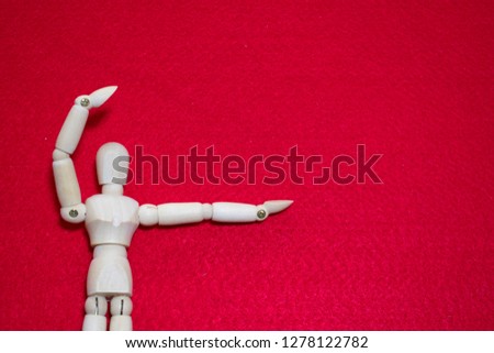 Wooden puppet hold up arm act like present something on red color acrylic background.