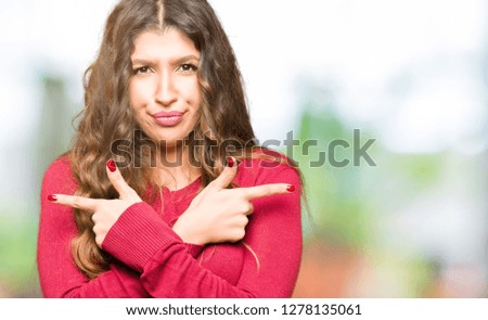 Young beautiful woman wearing red sweater Pointing to both sides with fingers, different direction disagree