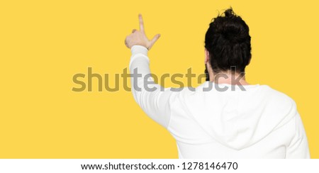 Young hipster man with long hair and beard wearing sporty sweatshirt Posing backwards pointing behind with finger hand