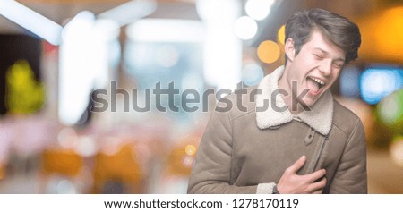 Young handsome man wearing winter coat over isolated background Smiling and laughing hard out loud because funny crazy joke. Happy expression.