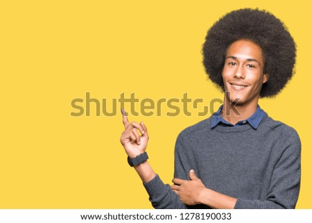 Young african american business man with afro hair with a big smile on face, pointing with hand and finger to the side looking at the camera.