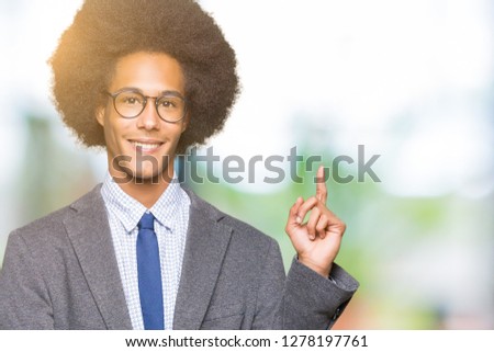 Young african american business man with afro hair wearing glasses with a big smile on face, pointing with hand and finger to the side looking at the camera.