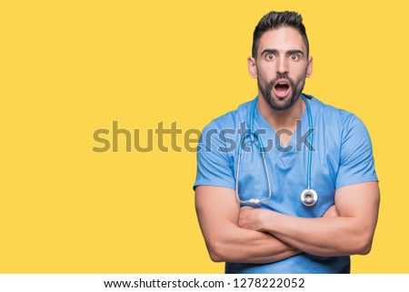 Handsome young doctor surgeon man over isolated background afraid and shocked with surprise expression, fear and excited face.