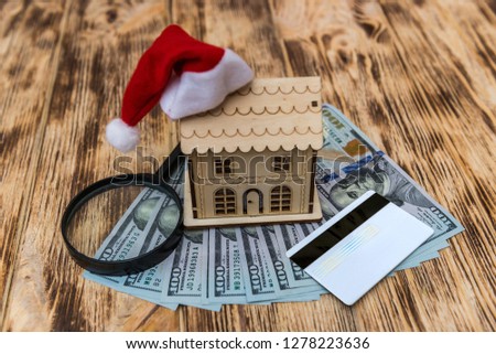 Wooden house model with santa hat and dollar banknotes