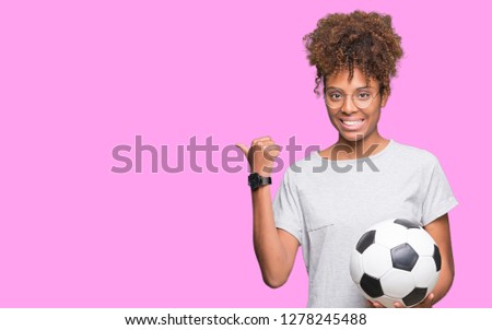Young african american woman holding soccer football ball over isolated background pointing and showing with thumb up to the side with happy face smiling