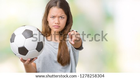 Young beautiful brunette woman holding soccer football ball over isolated background pointing with finger to the camera and to you, hand sign, positive and confident gesture from the front