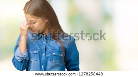 Young beautiful brunette woman wearing blue denim shirt over isolated background tired rubbing nose and eyes feeling fatigue and headache. Stress and frustration concept.