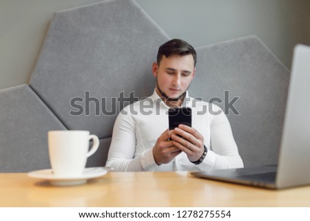 Portrait of Young man with a mobile phone sitting at cafe using laptop.