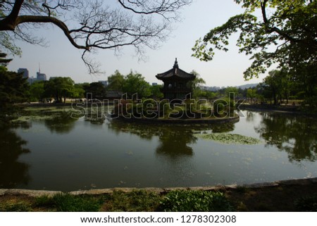 In the center of the lake there is an island of an ideal round shape on which the pagoda stands. In the background are visible high-rise buildings of the metropolis.