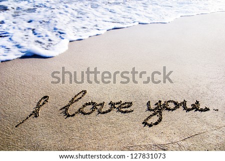 words "I love you" outline on the wet sand with the wave brilliance
