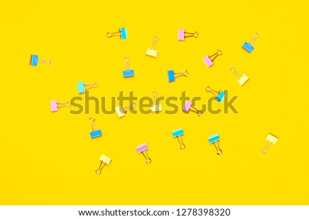 Multicolored paper clips on bright yellow background top view flat lay copy space. Minimalistic office background, education, objects for creativity. Back to school concept.