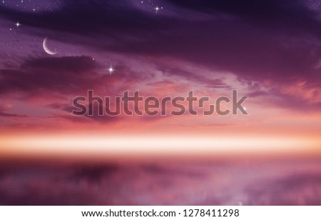 Amazing sunset picture with fluffy clouds, crescent moon against bright rays of sun reflected on the water surface.