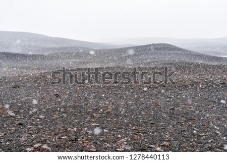 East Iceland highlands with barren brown landscape with summer snowing snow storm flakes falling weather and gray mountain