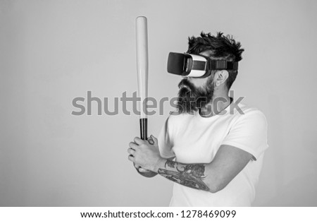 Man with bushy beard and tattoo holding green bat. Hipster with trendy beard and mustache doing sports. Bearded man in VR goggles learning to play baseball with 3D video tutorial, fitness concept.