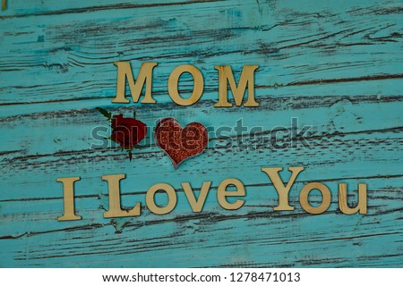 Lettering Mom I Love You in wooden letters with red heart and red rose on turquoise blue background of old wood