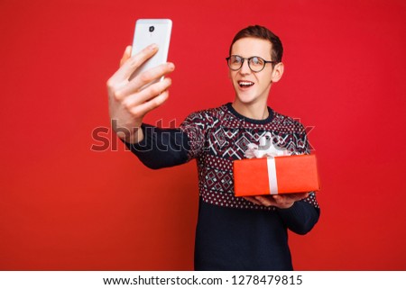 A man in glasses, with a gift in his hands, photographs himself on a smartphone