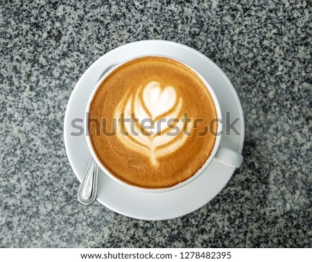 Heart shaped cappuccino cream coffee in the white coffee cup on the gray table top view.   