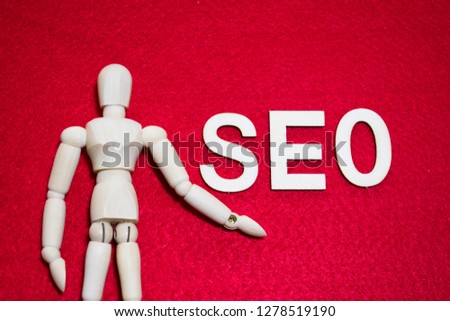 Search Engine Optimization (SEO) Concept, Wooden puppet reach out one’s hand to SEO wooden letters with red color acrylic felt in the background.