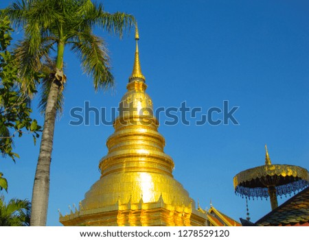 Golden pagoda in the Buddhist temple and palm tree with blue sky in Wat Phra That Hariphunchai located in LamPhun Province, Thailand.