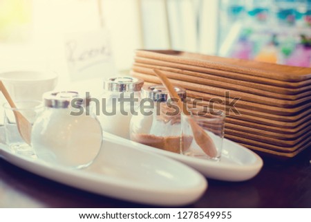 cream for coffee with white and red sugar in a glass jar with wooden trays on shelves in cafe, selective focus