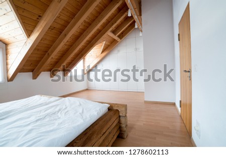 bright light modern simple master bedroom with wooden parquet floors and designer closet and traditional wooden beam bed under slanted ceiling in a refurbished apartment Royalty-Free Stock Photo #1278602113