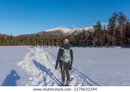 a photographer takes a picture of a woman standing on a frozen lake in the White Mountains of New Hampshire located in the United States