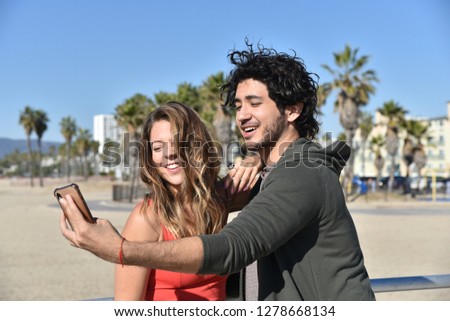 Romantic young couple taking cell phone pictures on a beach on vacation