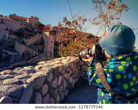 Young traveler photographer in Greek Meteora. 2 year old boy takes pictures of the stunning landscape of mountains and monasteries on a reflex camera.
