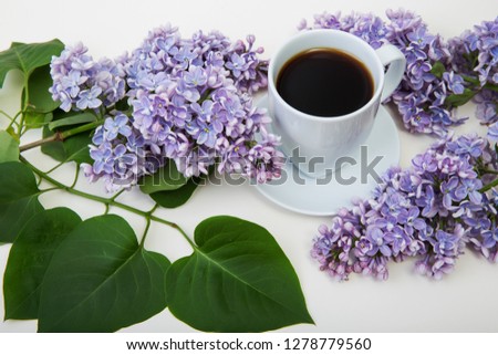 Blooming lilac and fresh coffee in a white cup.