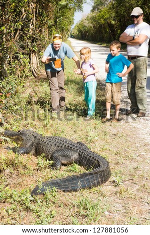 Family with two children, tourists photographing a large alligator on the phone
