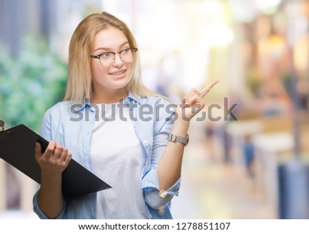 Young caucasian business woman holding clipboard over isolated background very happy pointing with hand and finger to the side