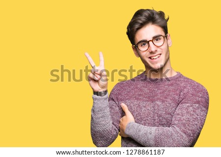 Young handsome man wearing glasses over isolated background smiling with happy face winking at the camera doing victory sign. Number two.