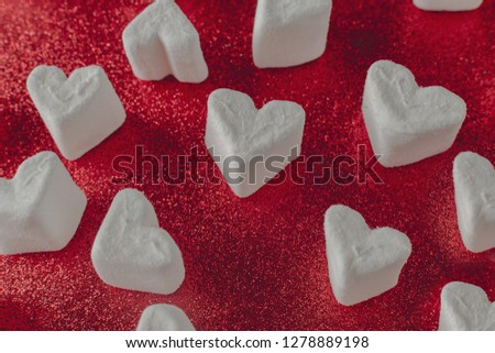 Valentines day minimal concept - pink and white heart marshmallows on glitter red background, copy space, top view,