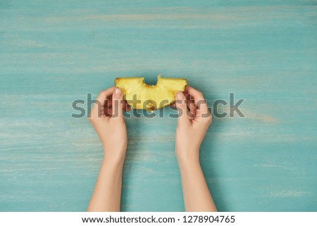 cropped view of woman holding yellow slice of pineapple on turquoise wooden table